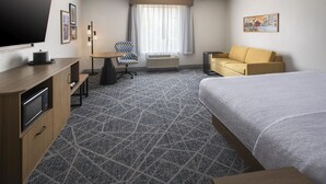 A hotel room with a bed, a sofa, a desk with a chair, a television, and a window with curtains. - Hampton Inn and Suites New Hartford/Utica (New Hartford)