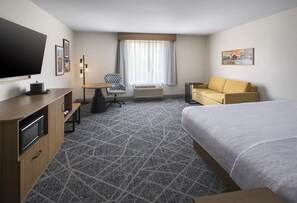 A hotel room with a bed, a sofa, a desk with a chair, a television, and a window with curtains. - Hampton Inn and Suites New Hartford/Utica (New Hartford)
