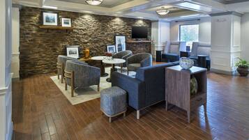 A modern living room with stone wall, multiple seating options, a flat-screen TV, and a large window.