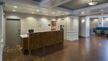 A hotel reception area with a wooden reception desk, a 'Welcome to the Empire State' sign, and a 'Hilton Honors' sign.