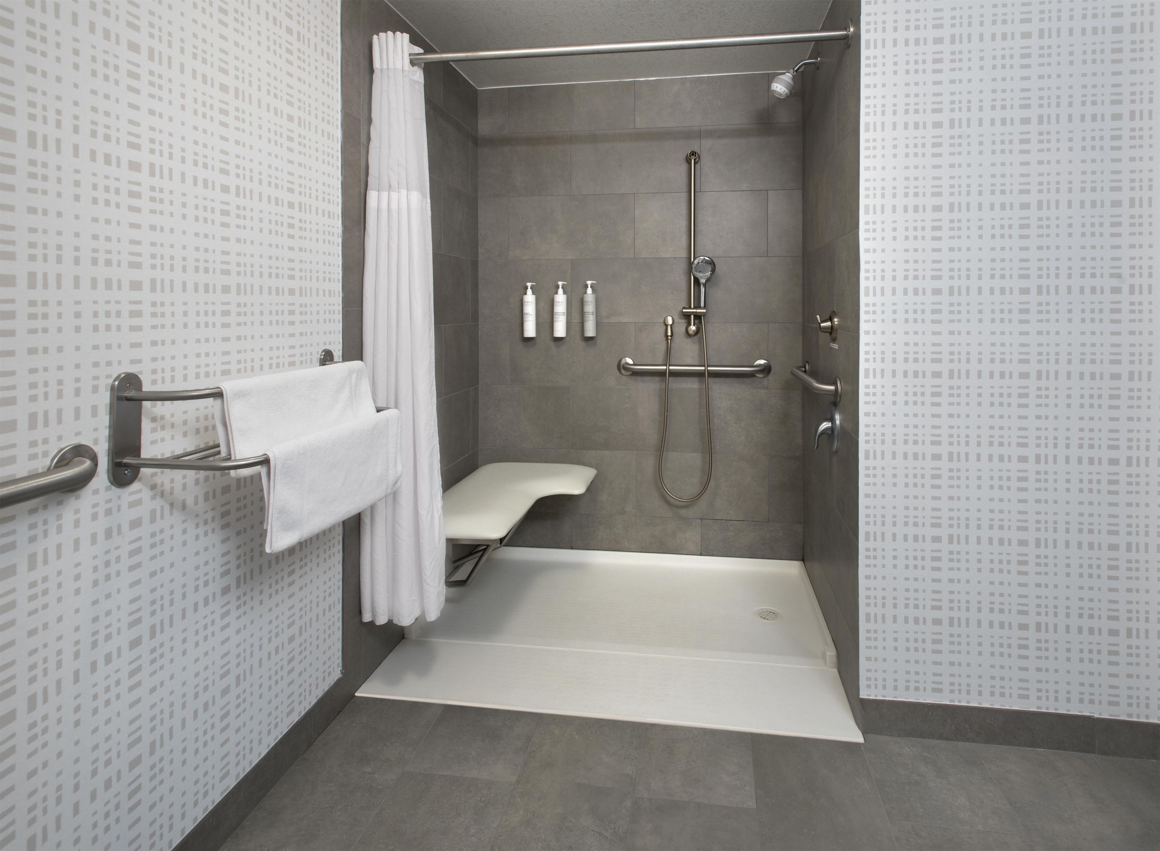A modern bathroom with a shower, toilet, and grab bars.