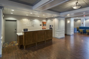 A hotel reception area with a wooden reception desk, a 'Welcome to the Empire State' sign, and a 'Hilton Honors' sign. - Hampton Inn and Suites New Hartford/Utica (New Hartford)