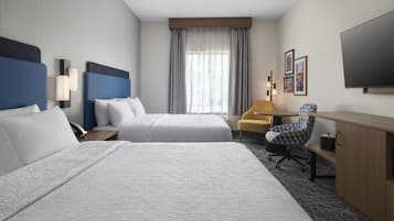 A hotel room with two beds, a desk, a chair, a television, and a window with curtains.