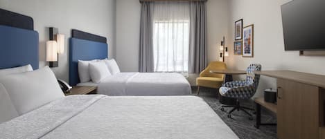 A hotel room with two beds, a desk, a chair, a television, and a window with curtains.