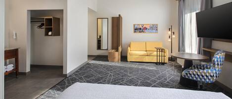 A hotel room with a bed, a sofa, a TV, a small table, and a chair.