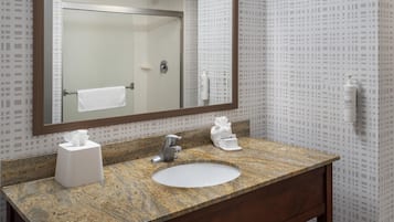 A bathroom with a granite countertop, a white sink, a mirror, and a towel rack.