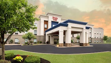 A Hampton Inn & Suites by Hilton building with a covered entrance, landscaped garden, and a parking lot.