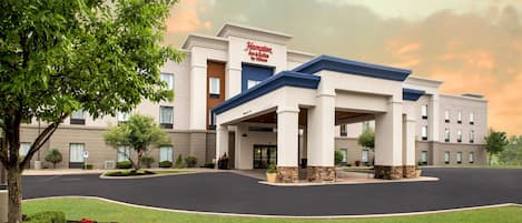 A Hampton Inn & Suites by Hilton building with a covered entrance, landscaped garden, and a parking lot.