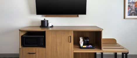 A compact hotel room with a wooden desk, a flat-screen TV, a microwave, and a coffee maker.