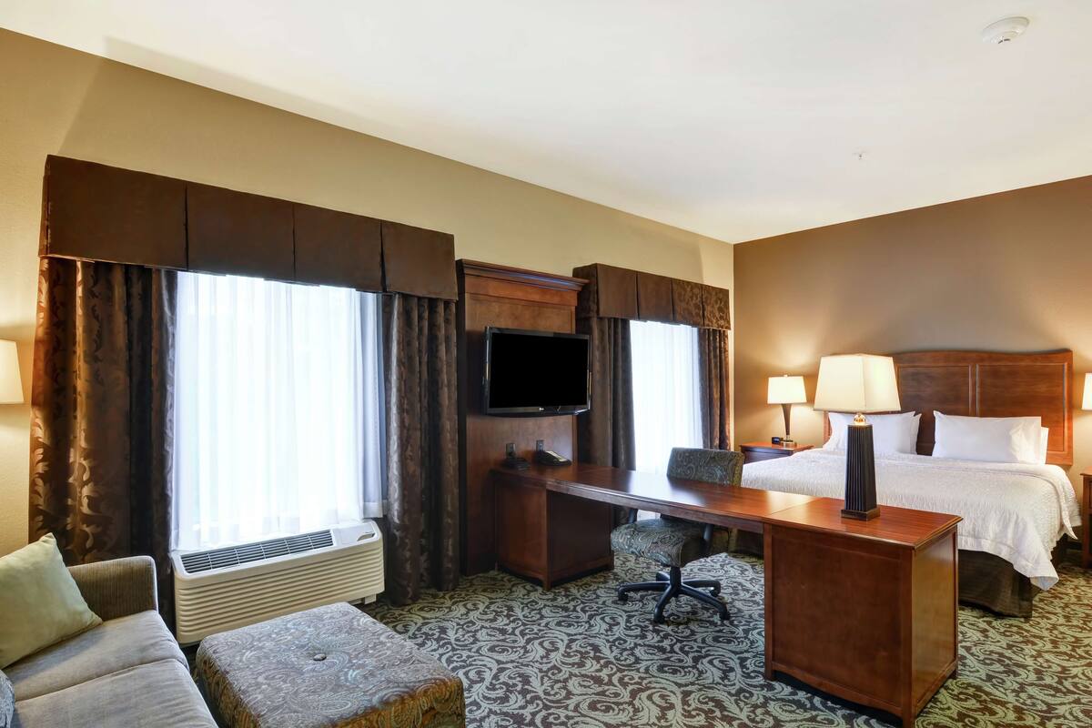 A hotel room with a bed, desk, chair, television, and a large window with curtains.