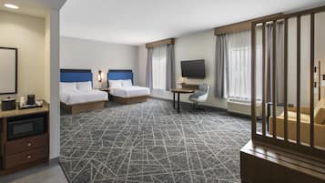 Quarto de hotel com duas camas, uma escrivaninha, uma cadeira, televisão e uma janela grande com cortinas.