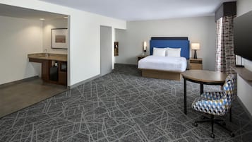 A hotel room with a bed, a desk, a chair, a TV, and a bathroom.