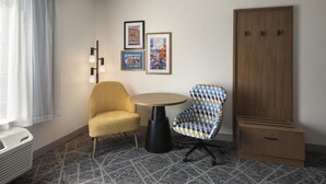 A hotel room with a yellow armchair, a patterned armchair, a small round table, a wardrobe, and two framed pictures on the wall. - Hampton Inn and Suites New Hartford/Utica (New Hartford)