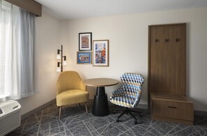 A hotel room with a yellow armchair, a patterned armchair, a small round table, a wardrobe, and two framed pictures on the wall. - Hampton Inn and Suites New Hartford/Utica (New Hartford)