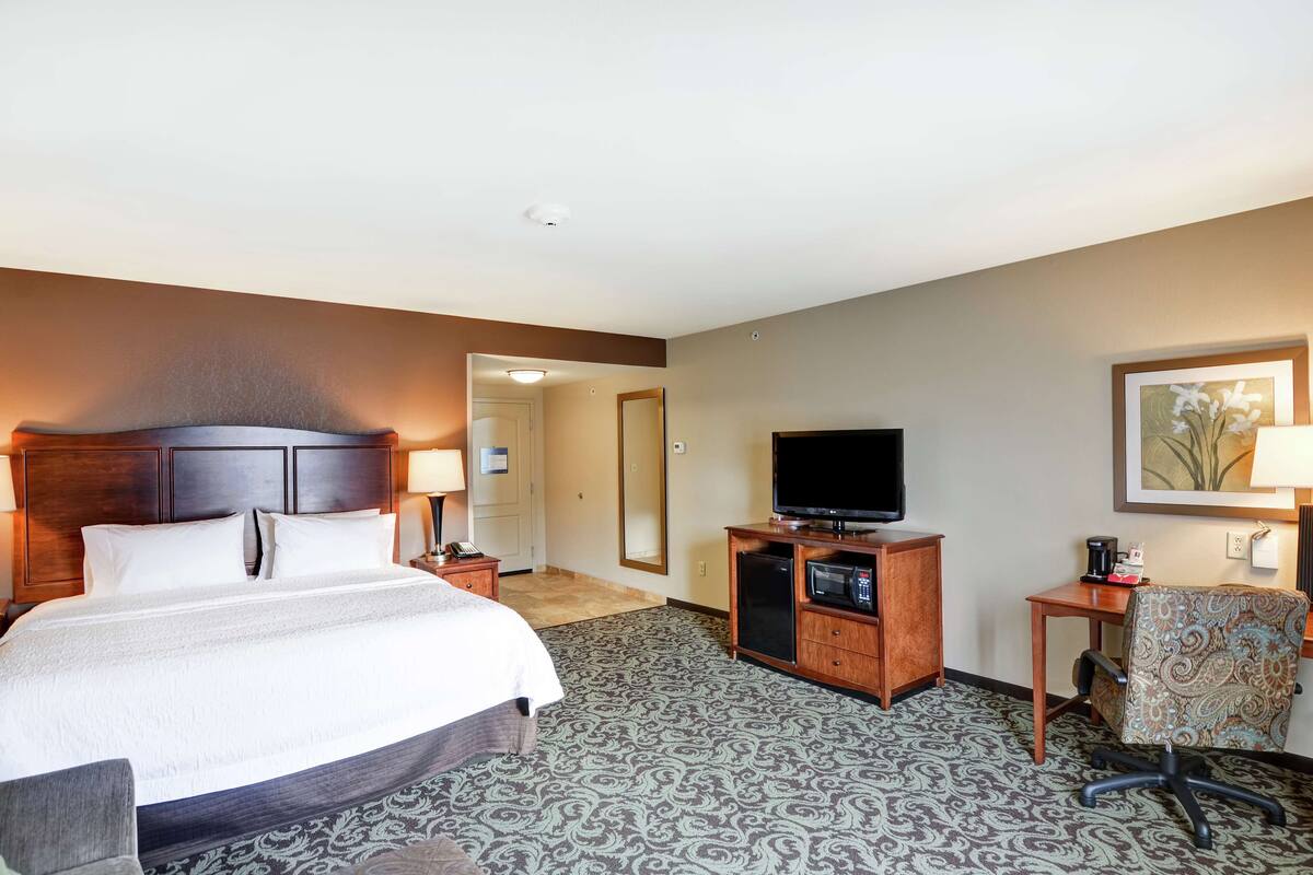 A hotel room with a large bed, a television, a desk with a chair, and a patterned carpet.