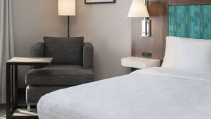 Une chambre d’hôtel avec un lit, une chaise, une petite table, deux lampes fixées au mur et un tableau encadré accroché au mur.