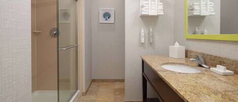 A bathroom with a glass shower enclosure, a sink with a granite countertop, and a mirror with a yellow frame.