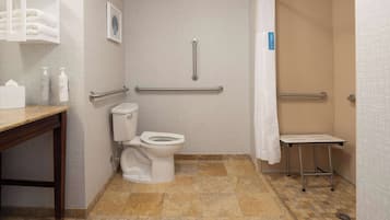 A bathroom with a toilet, a sink, a shower with a grab bar, and a small table.
