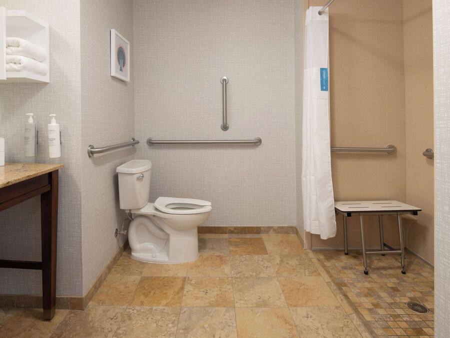 A bathroom with a toilet, a sink, a shower with a grab bar, and a small table.