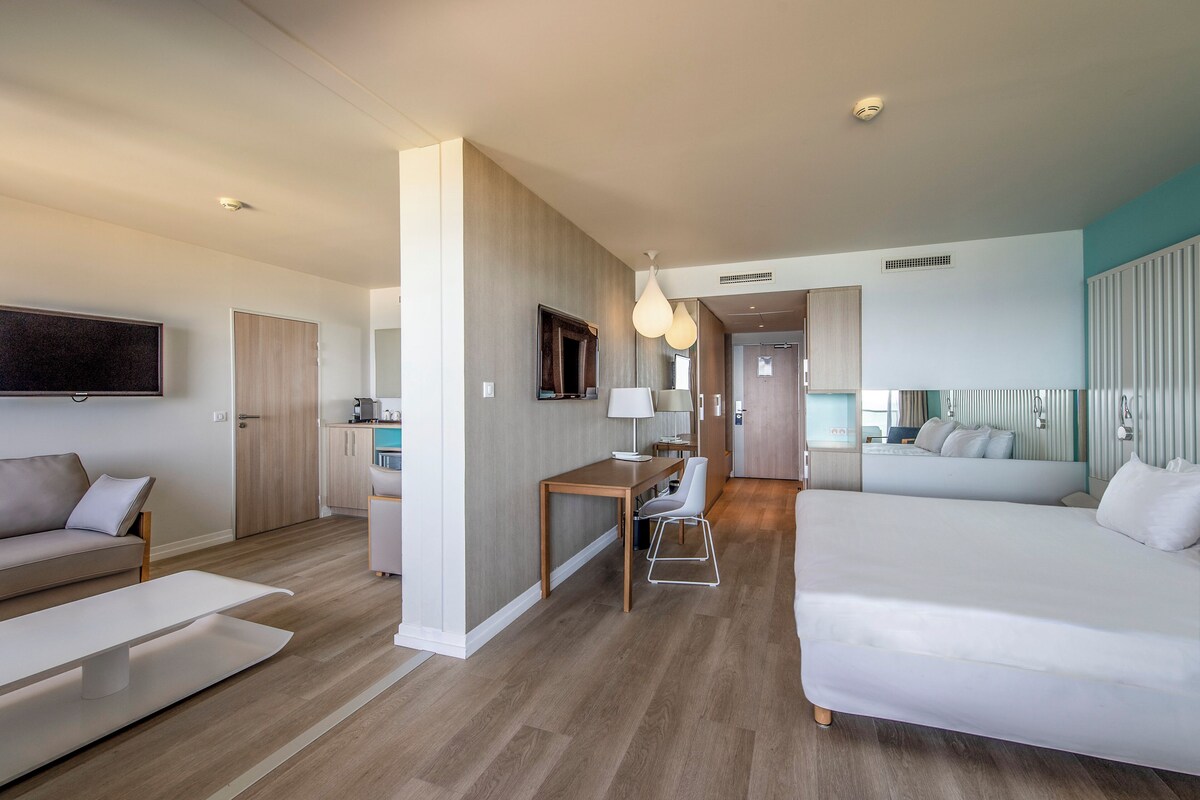 A modern hotel room with a bed, a desk, a chair, a sofa, and a TV.