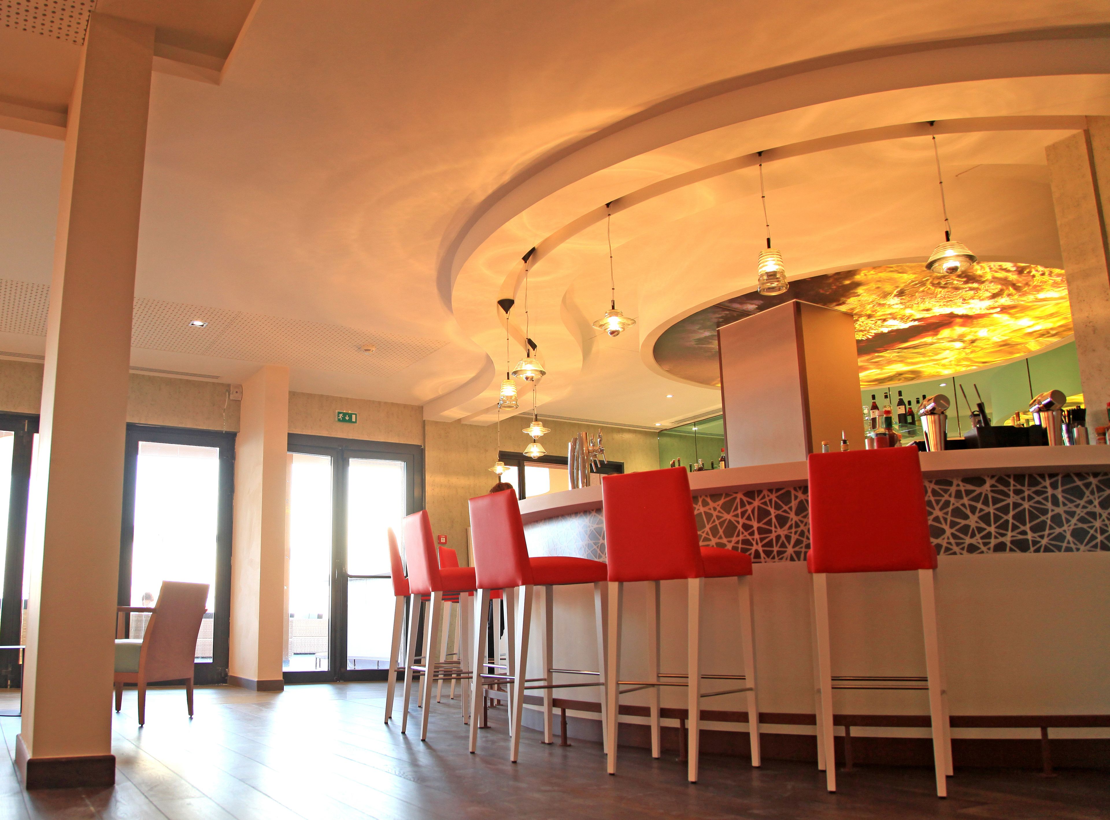A bar area with red chairs, a counter with a decorative backsplash, and hanging pendant lights.