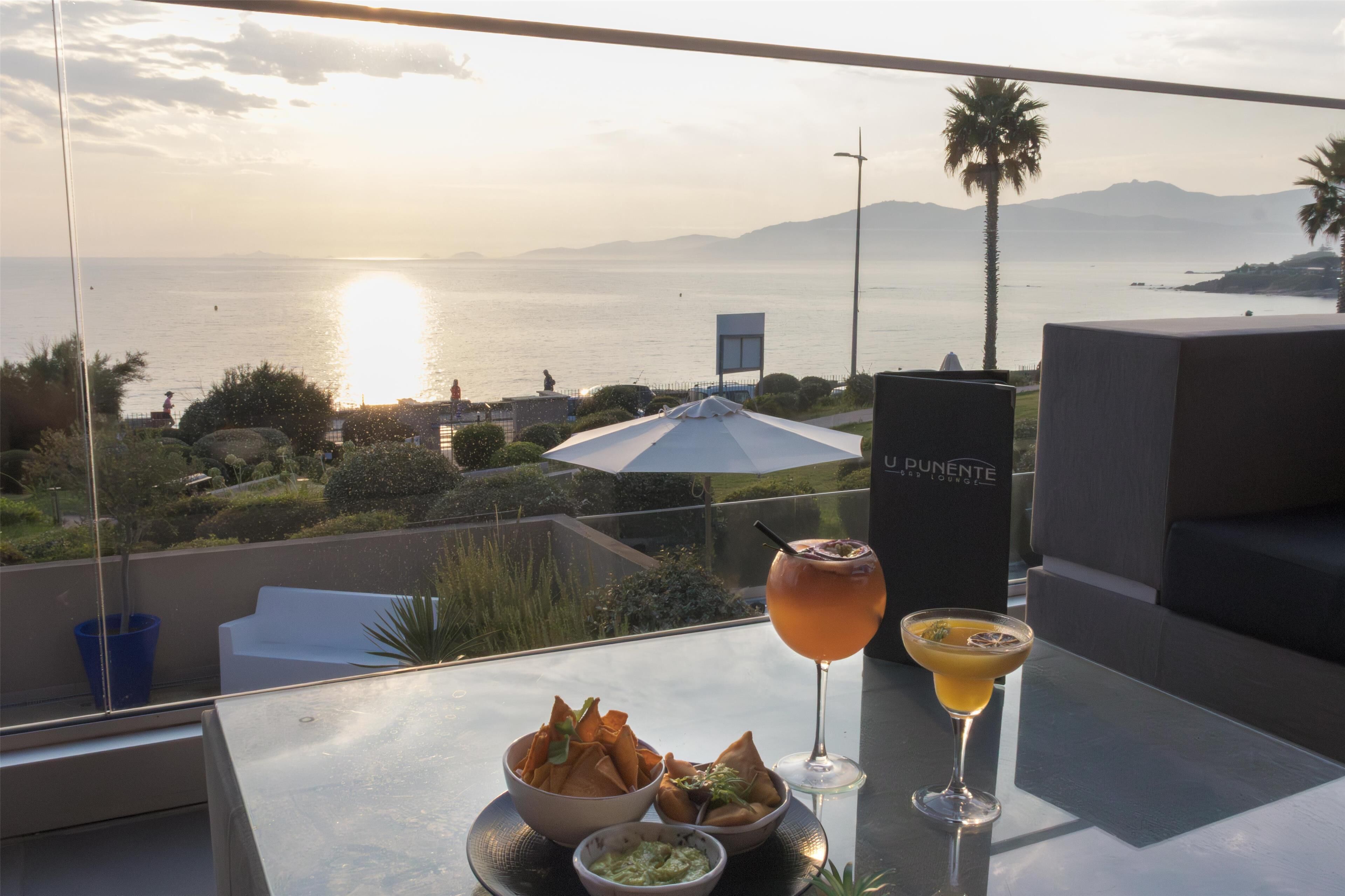Een tafel met lekkernijen, een drankje en uitzicht op de oceaan bij zonsondergang.