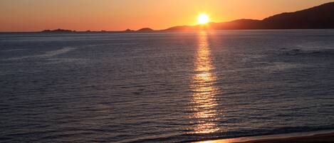 A sunset over a calm sea with distant landforms.