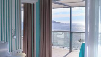 Una camera d'albergo con un letto, un comodino, una finestra con tende e vista sul mare.