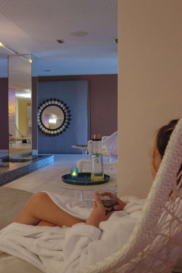 A person relaxing in a wicker chair with a towel, a glass of water, and a tray with candles and a bottle on the floor. - Radisson Blu Resort & Spa Ajaccio Bay (Albitreccia)