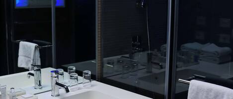 Une salle de bain moderne avec une douche à parois de verre, un grand miroir et un lavabo blanc agrémenté d’articles de toilette.