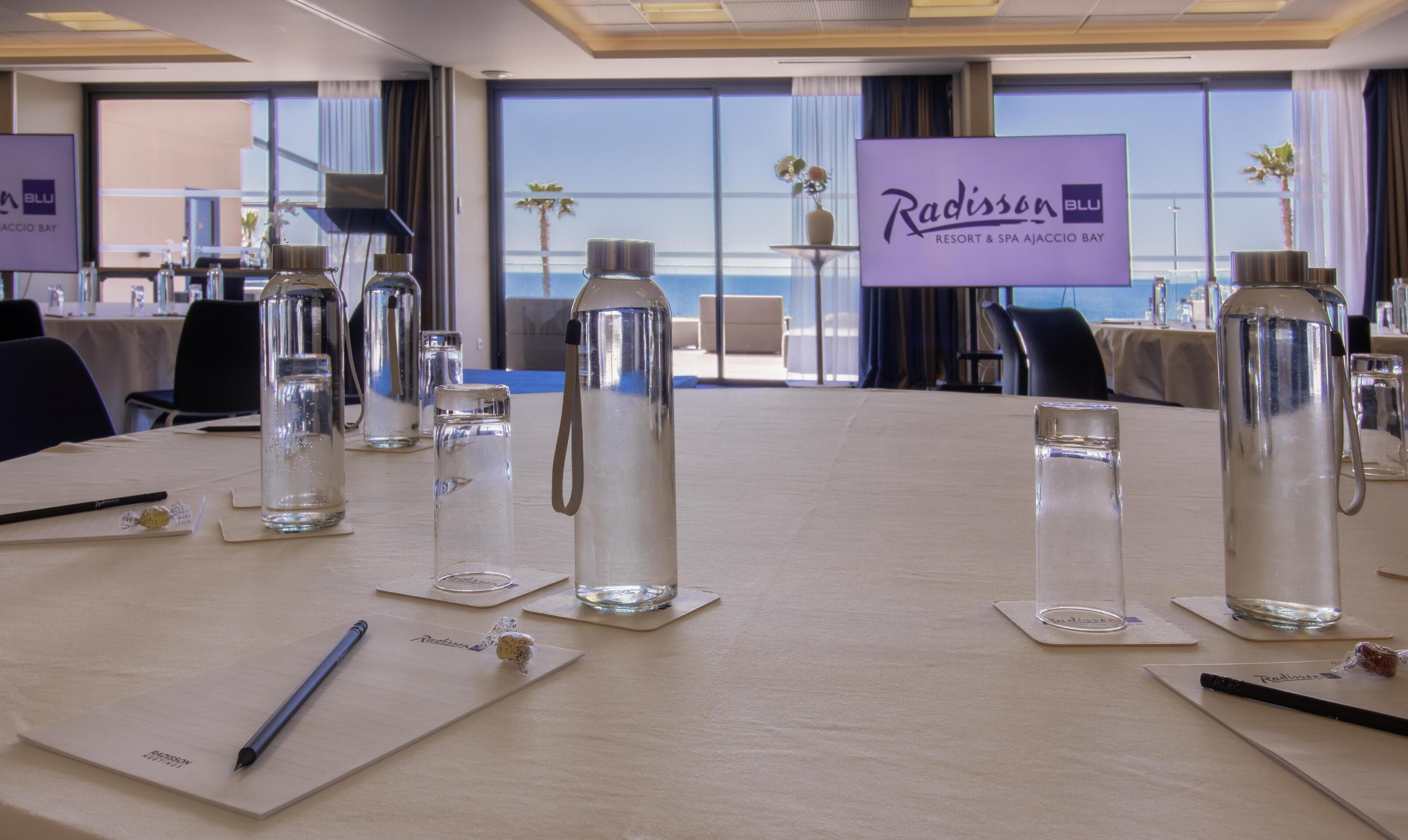 Un salón de conferencias con vistas al mar, botellas de agua y tarjetas de identificación para Radisson BLU Resort & Spa Ajaccio Bay.