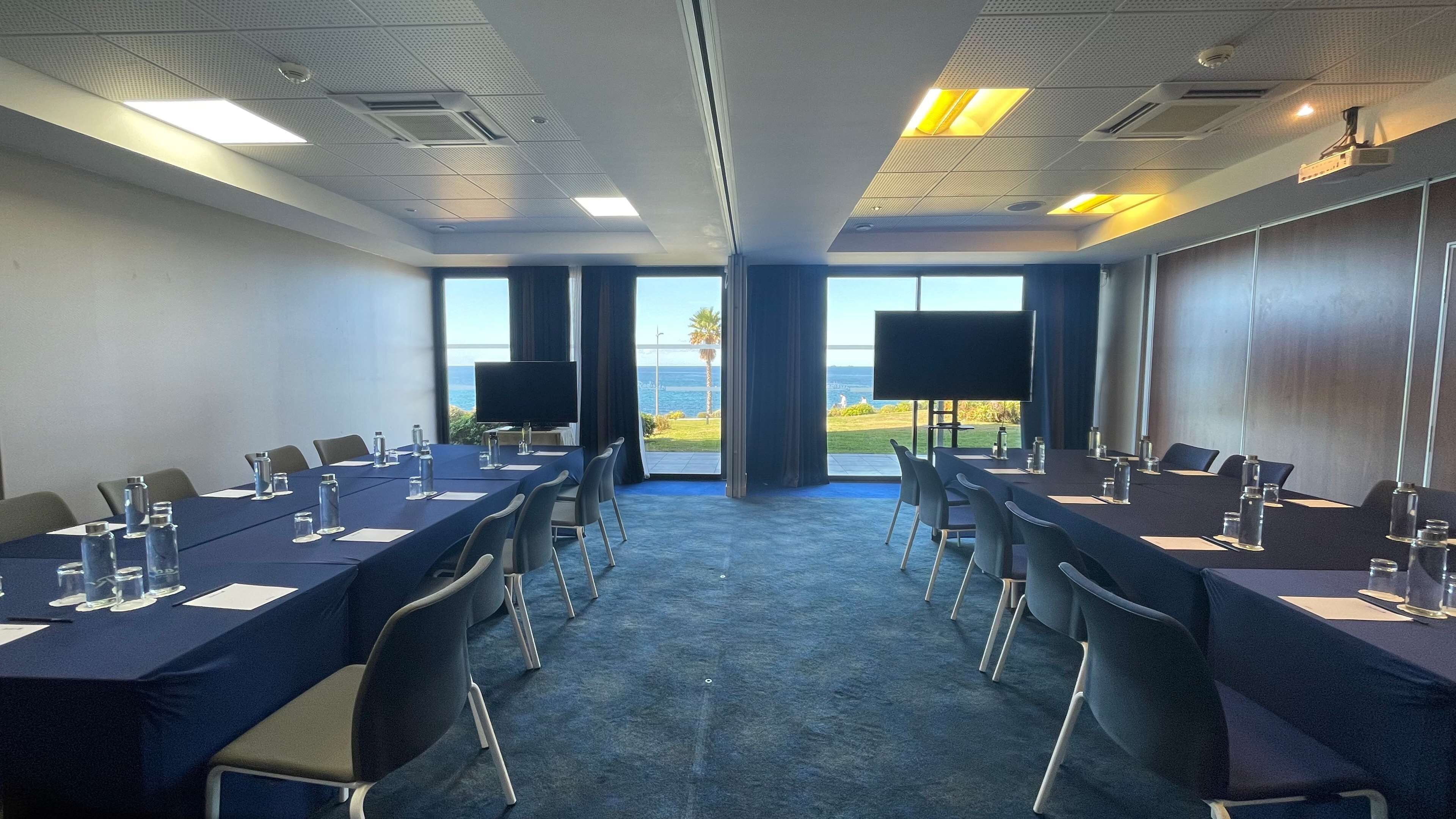 Een vergaderruimte met een lange tafel, stoelen, een groot scherm en uitzicht op de oceaan.