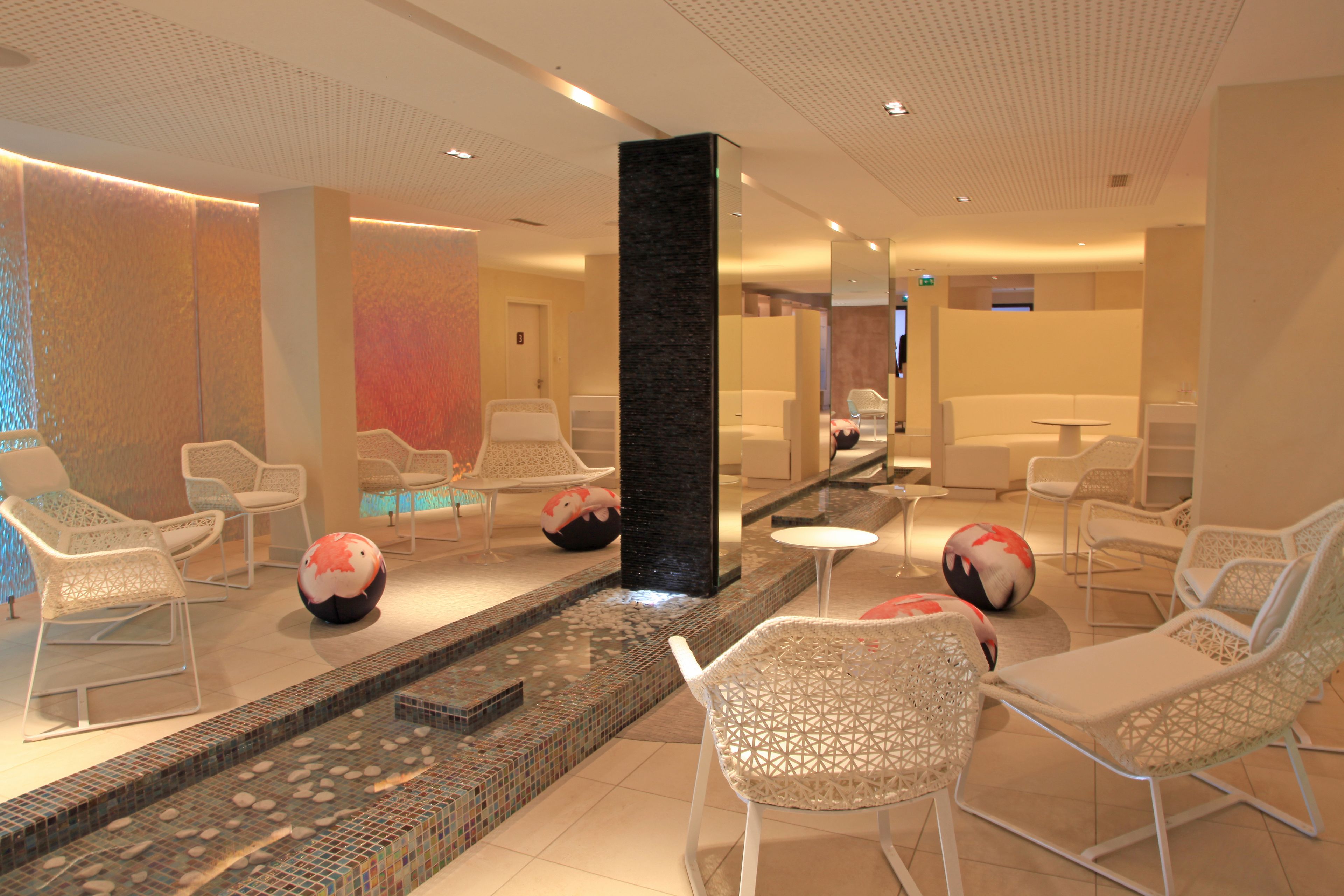 A modern lounge area with white chairs, a small pool, and decorative balls.