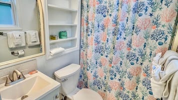 A bathroom with a white sink, a toilet, a shower curtain with a floral pattern, and a mirror with lights above it.