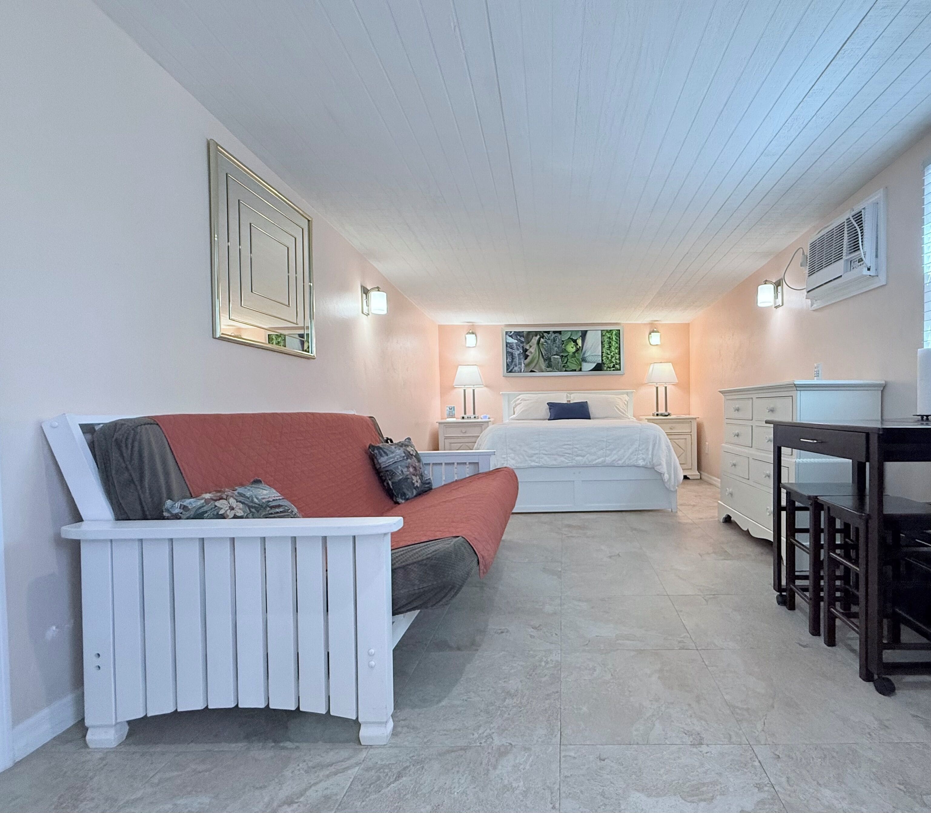 Une chambre à coucher avec un lit, un canapé blanc, une commode et une petite table.