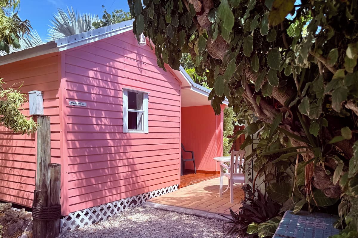A pink building with a window, a wooden post, and a patio area with a table and chairs.
