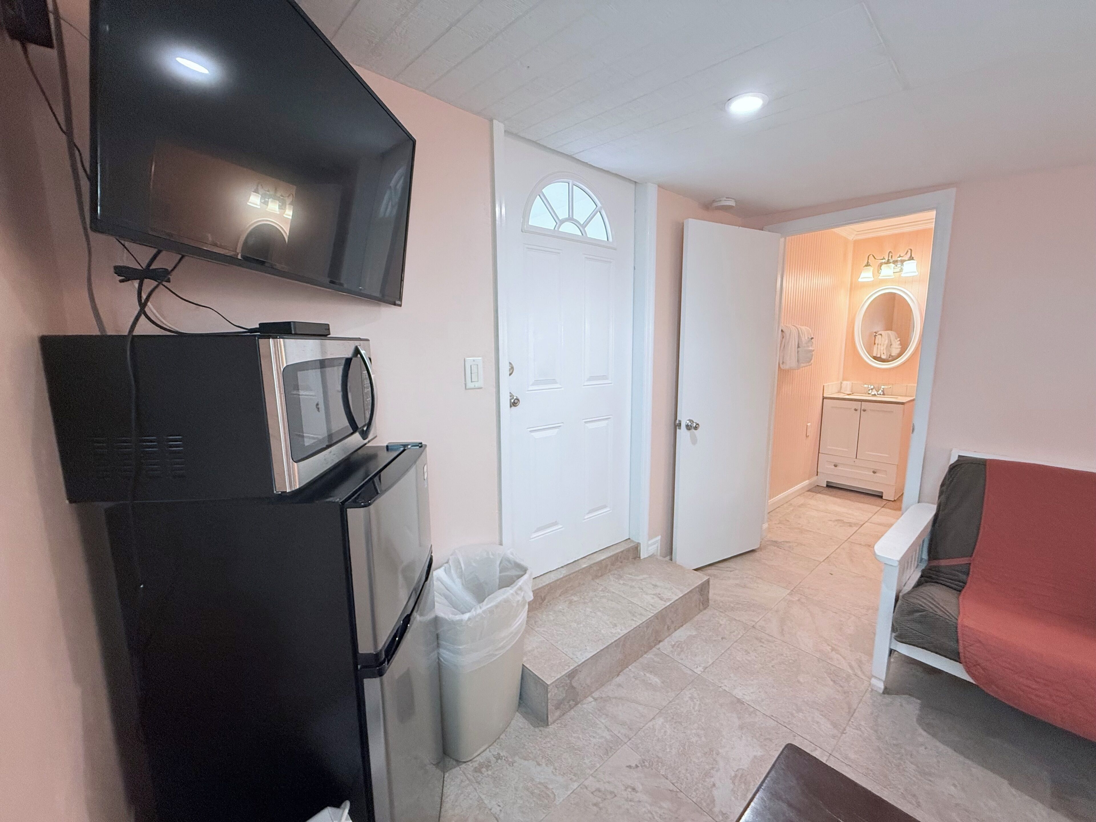 Un espace de vie compact comprenant un coin cuisine, un téléviseur, une porte donnant accès à une salle de bain et un canapé rouge.