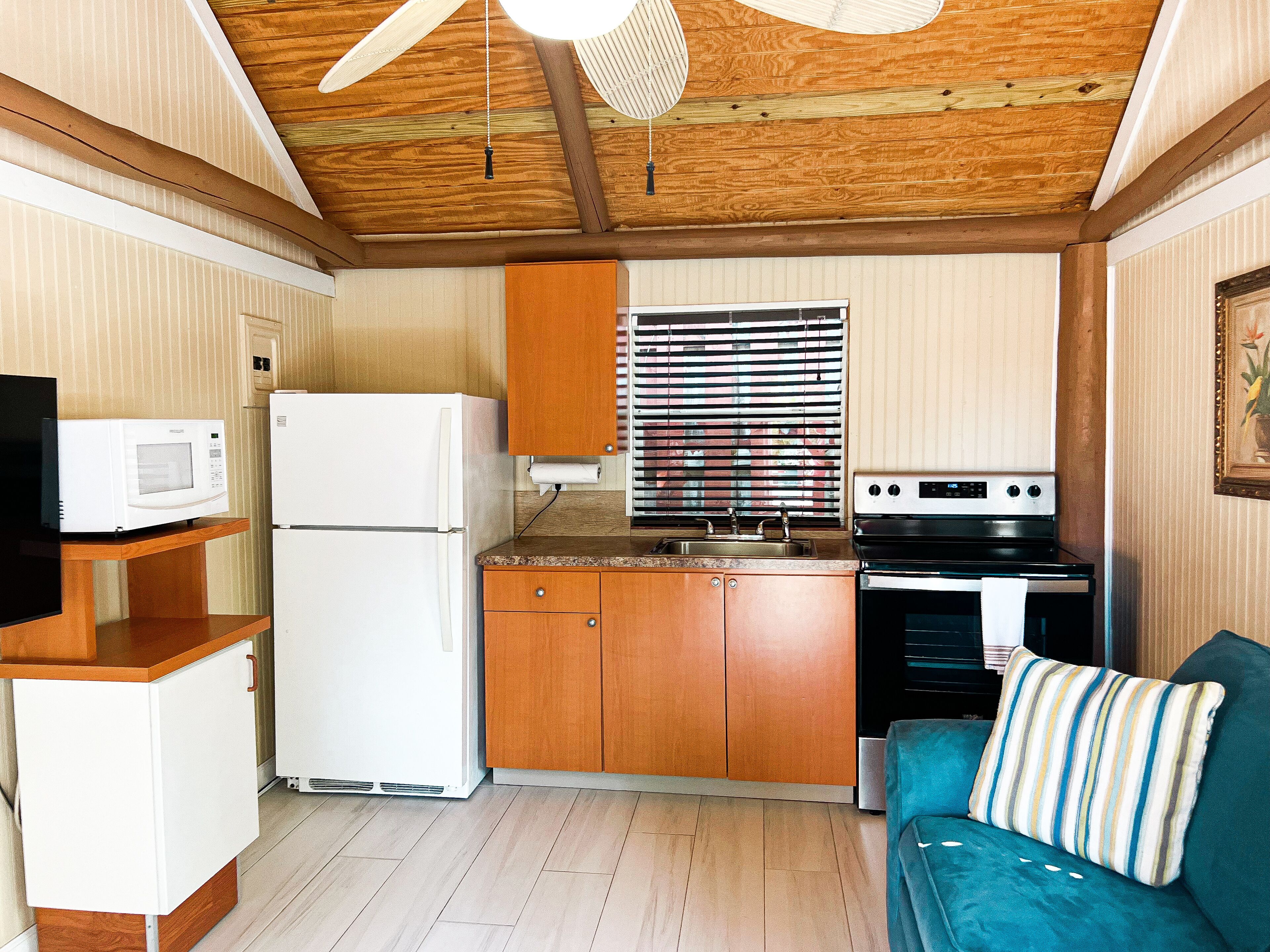 A compact kitchen with a microwave, refrigerator, stove, and wooden cabinets.