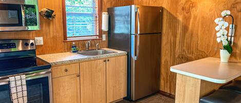 A kitchen with wooden cabinets, a stainless steel refrigerator, a microwave, and a sink.