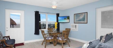 Una habitación con una mesa de comedor, sillas, un sofá, un ventilador de techo, un televisor y una ventana con vista al mar.