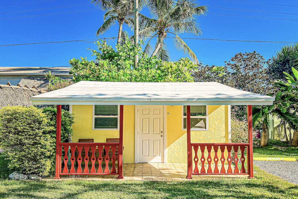 A small yellow building with a white door, red railings, and a tiled roof.
