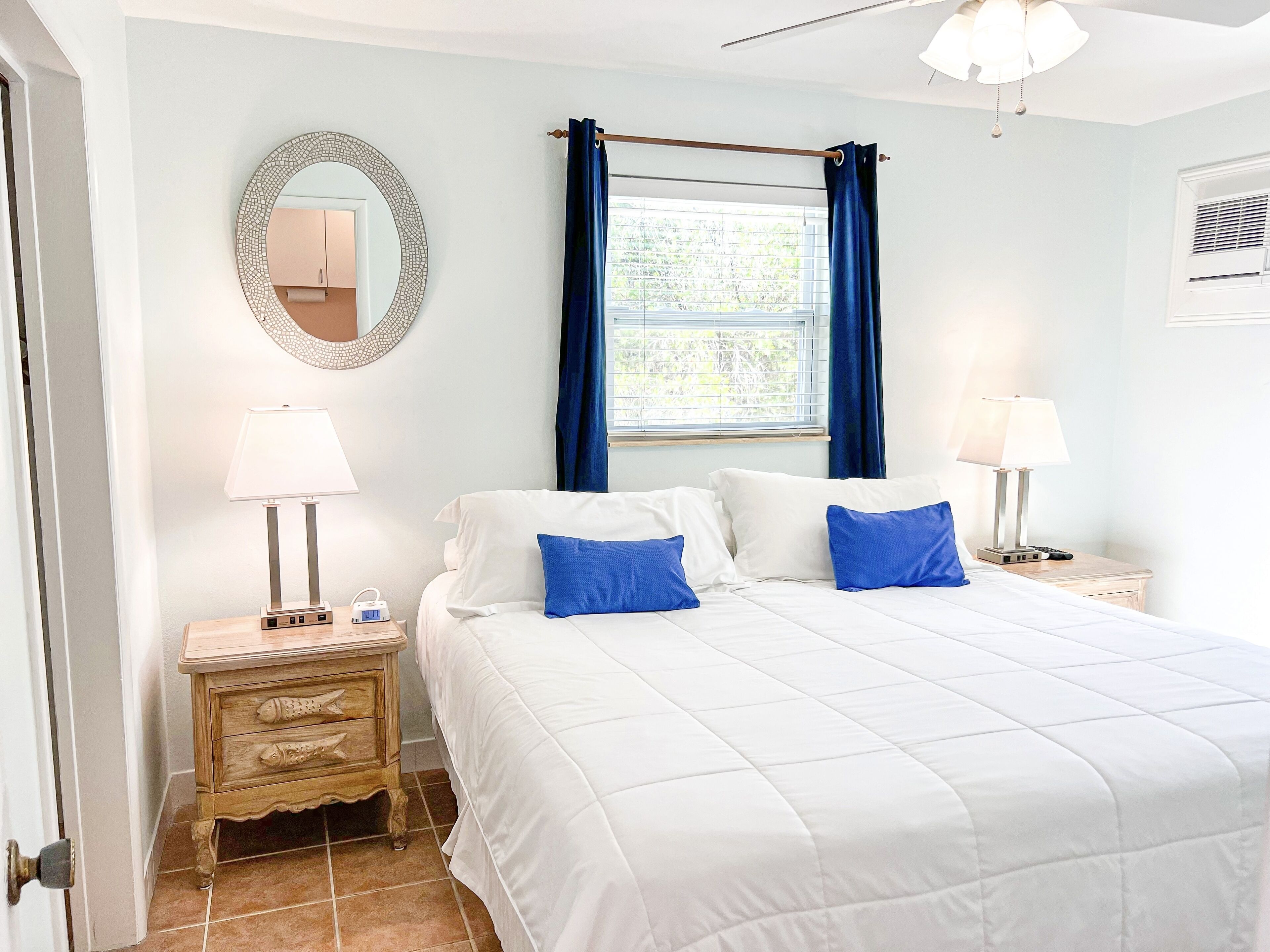 A bedroom with a bed, two bedside tables with lamps, a dresser, a mirror, and a window with curtains.