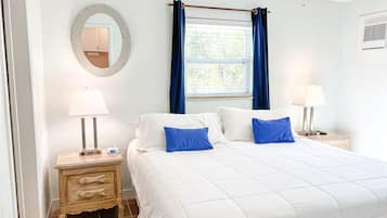 A bedroom with a bed, two bedside tables with lamps, a dresser, a mirror, and a window with curtains.