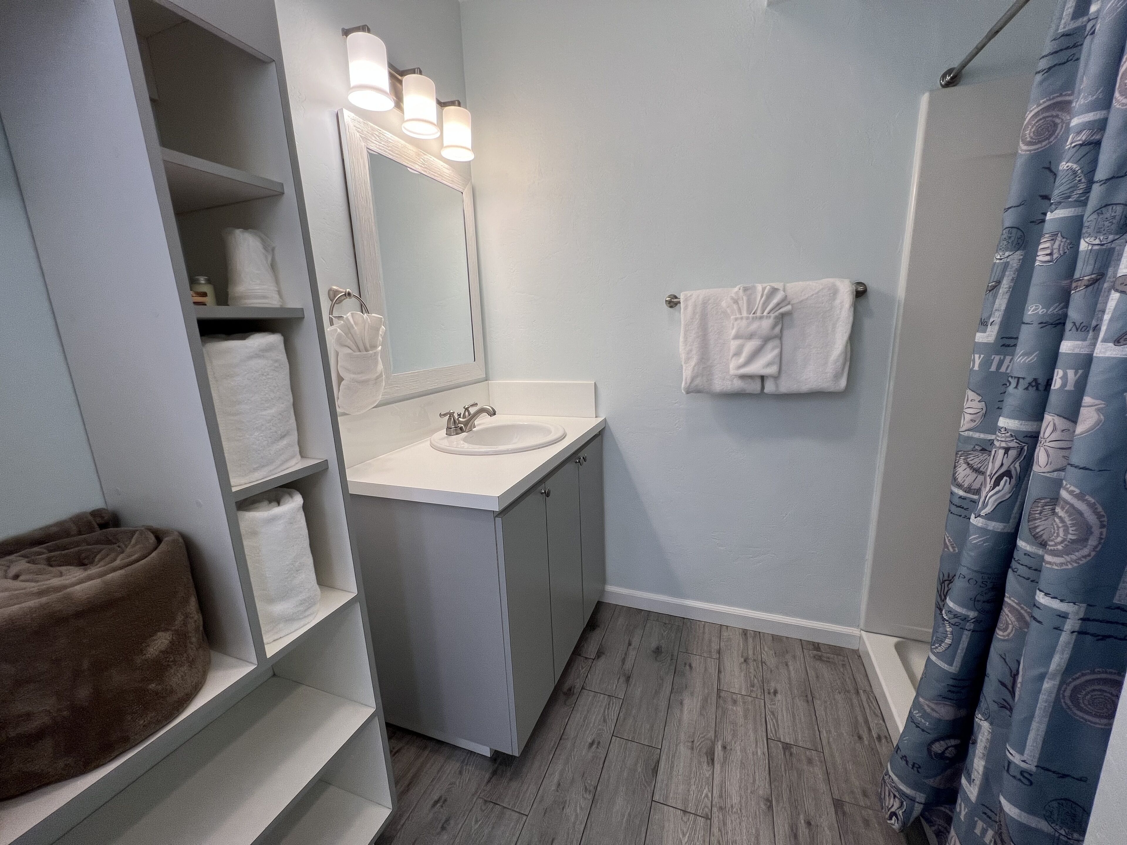 A bathroom with a white sink, mirror, and towel rack. There is a shower curtain with a nautical pattern.
