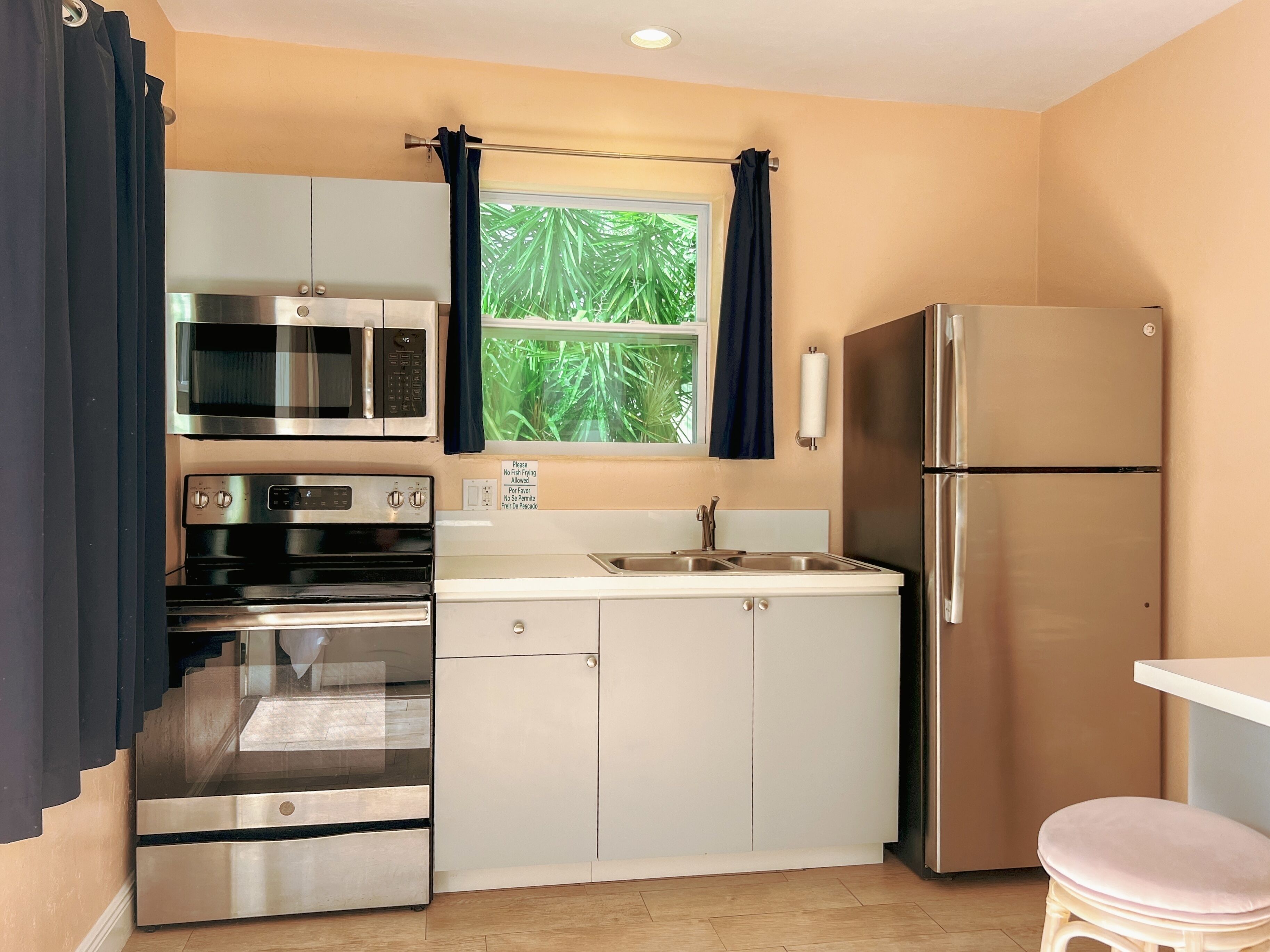 A compact kitchen with stainless steel appliances, a window with curtains, and a sink.