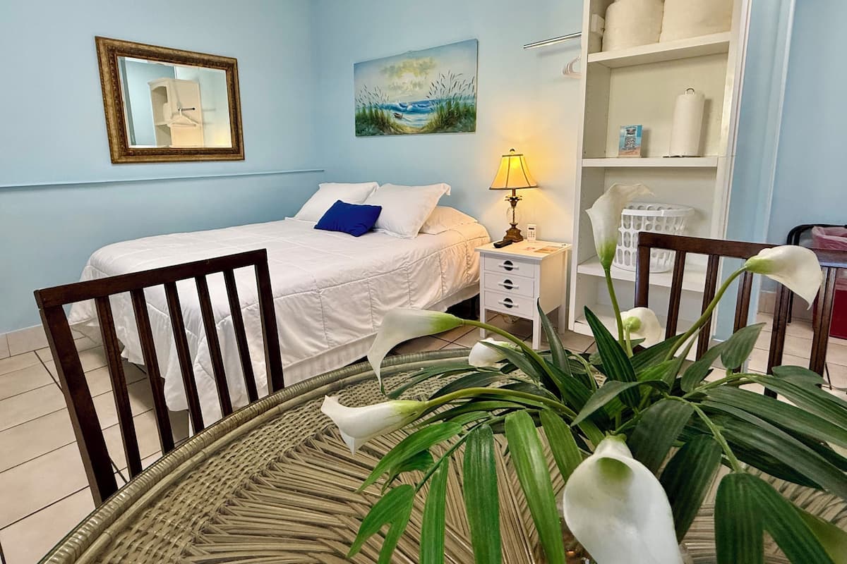 A bedroom with a bed, bedside table, lamp, and a shelf with towels.