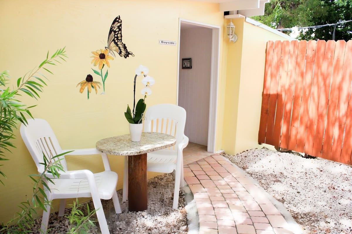 A patio with a round table, two white chairs, a potted plant, and a butterfly decoration on the wall.