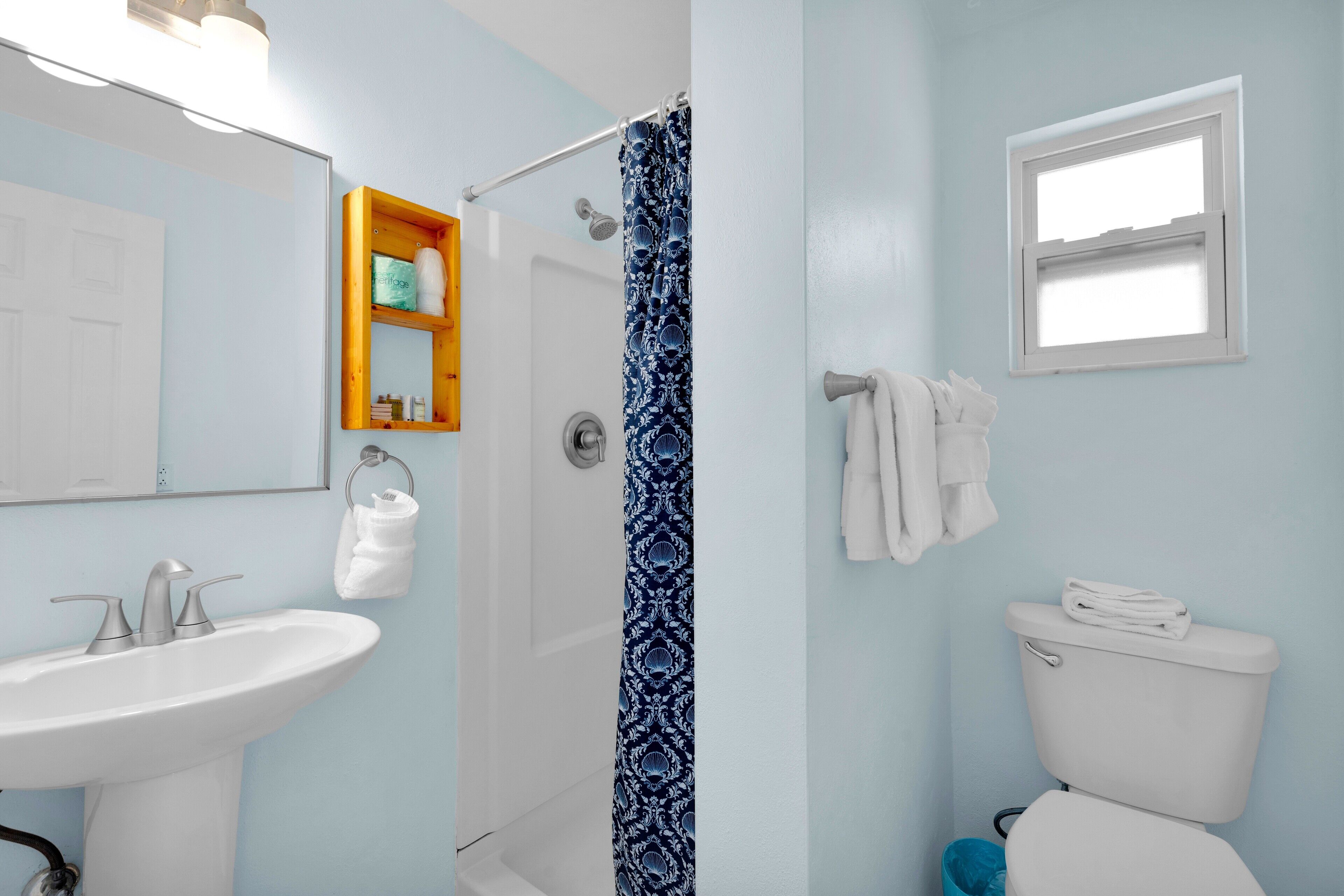 A bathroom with a white sink, a shower curtain, a toilet, and a window.