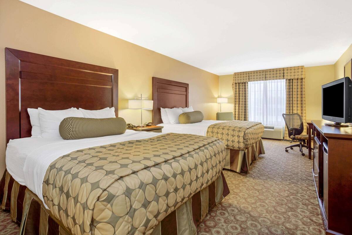 A hotel room with two beds, a television, and a desk.