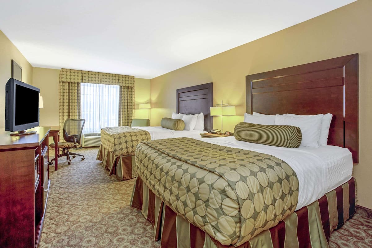 A hotel room with two beds, a desk with a television, and a chair.